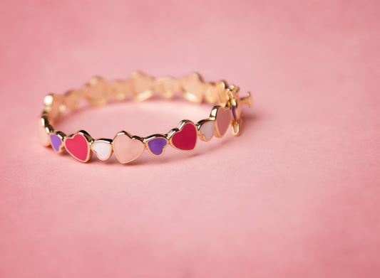 Gold bracelet with colorful heart-shaped charms on a pink background