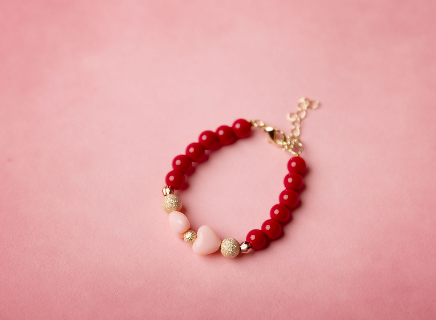 Red beaded bracelet with gold and pink accents on a pink background
