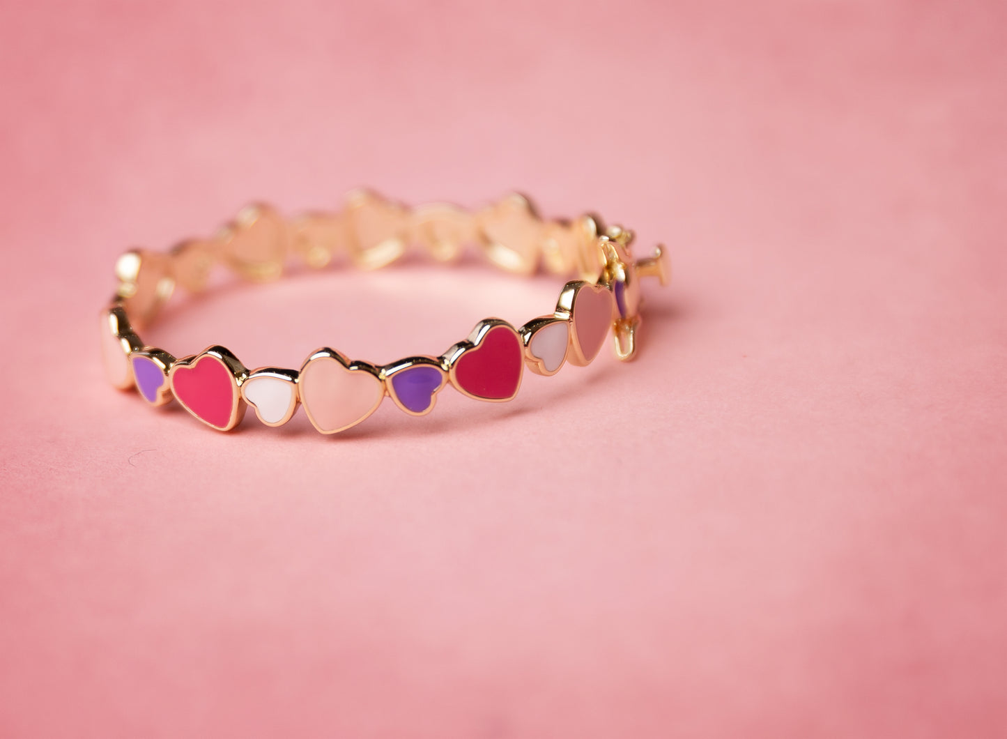 Gold bracelet with colorful heart-shaped charms on a pink background